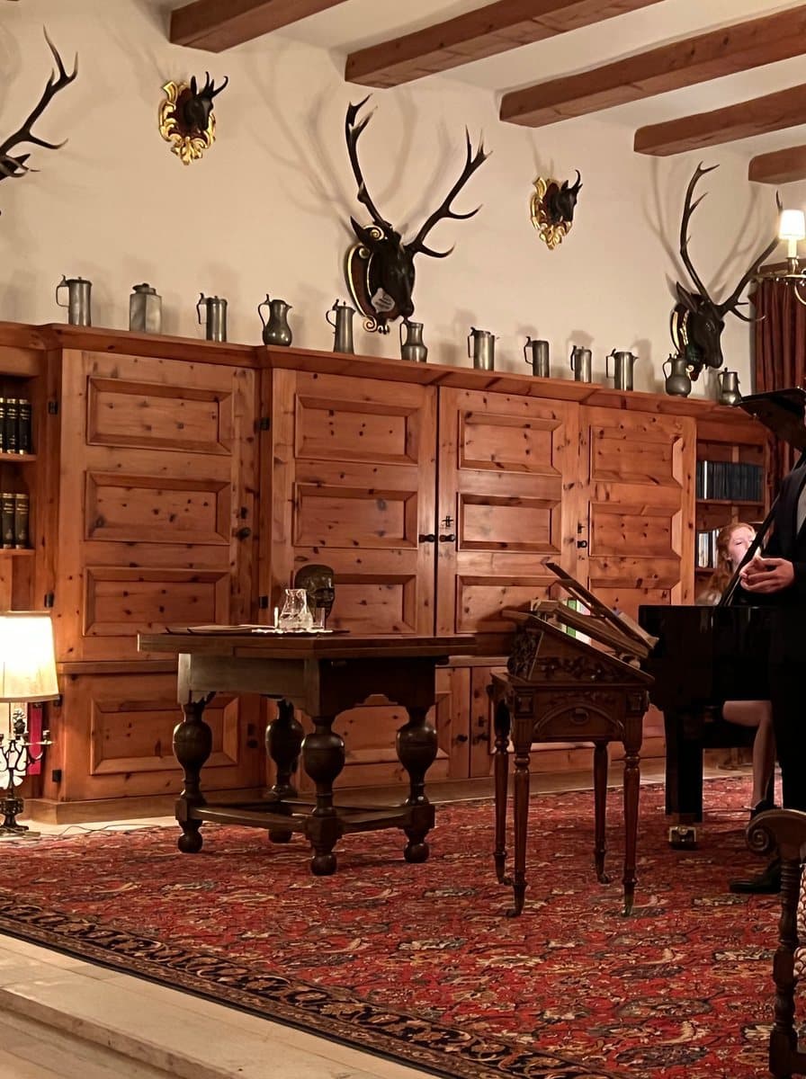 A panelled hall with antler trophies, a brass chandelier and a grand piano