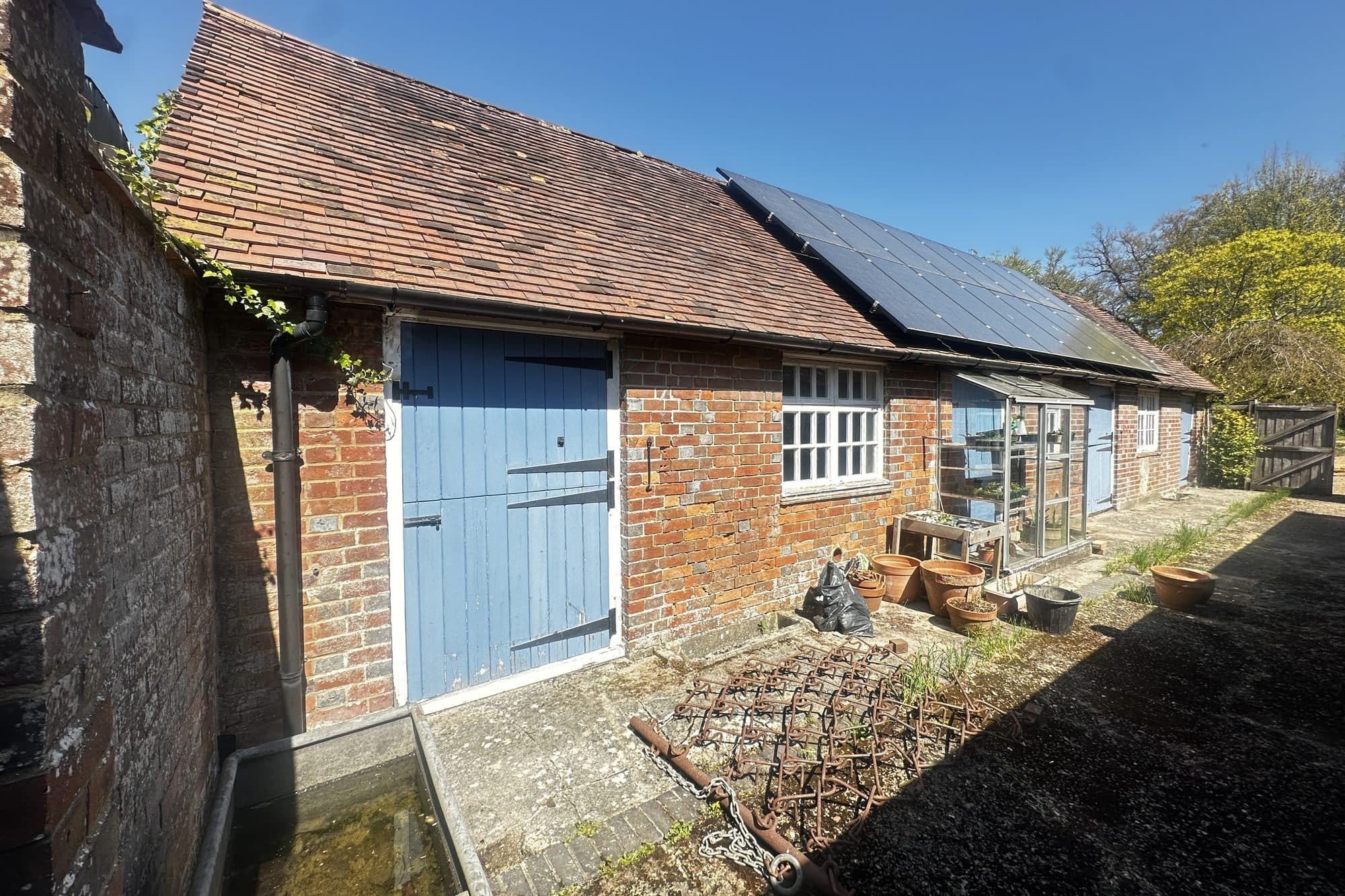 The barn's courtyard side in sunshine, with blue stable doors, white casements and a greenhouse