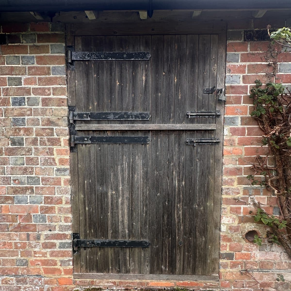 A weathered ledged timber door with long iron strap hinges in a brick wall
