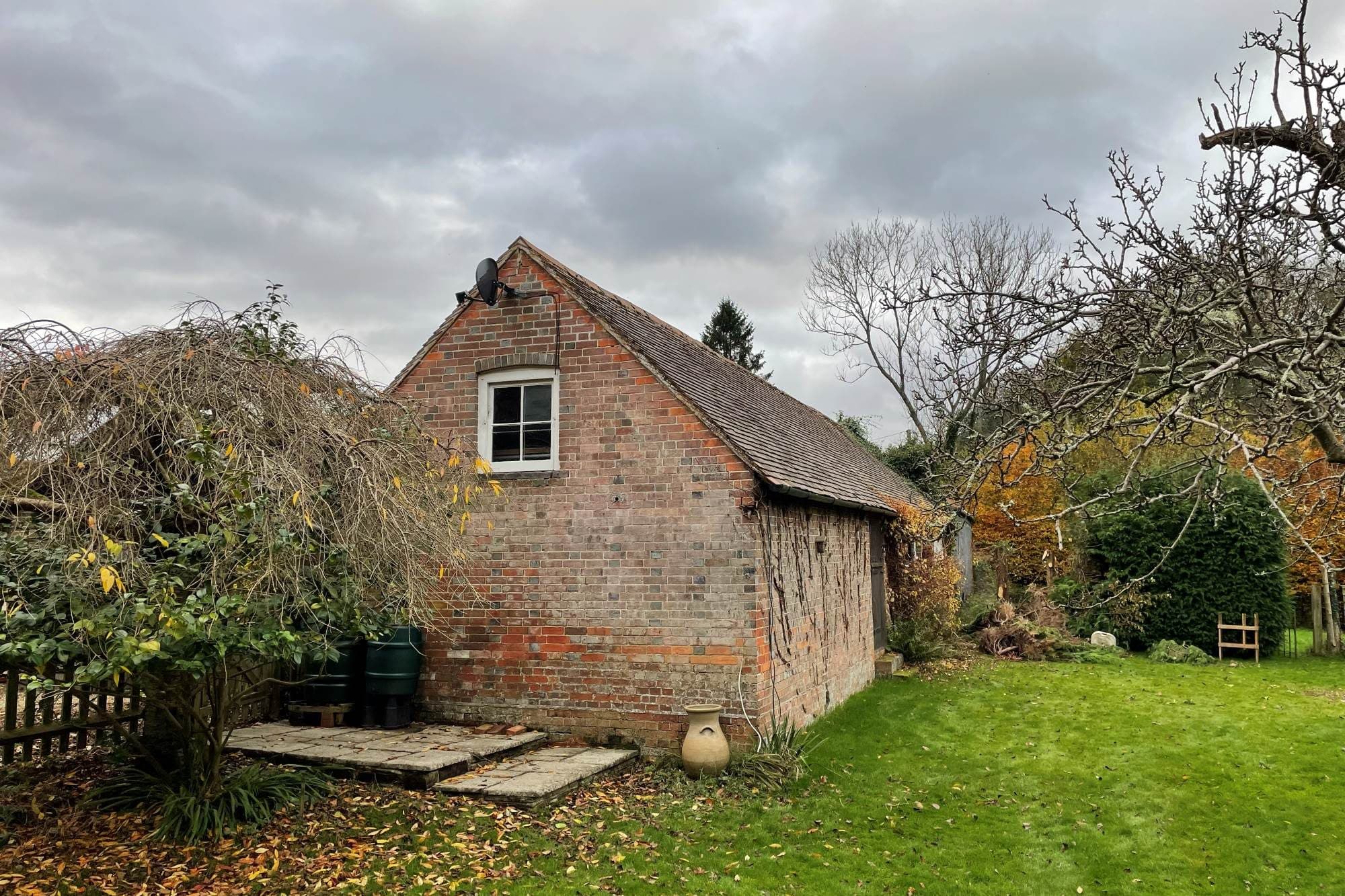 The brick gable end of the barn with a chimney and a small white window, among autumn trees