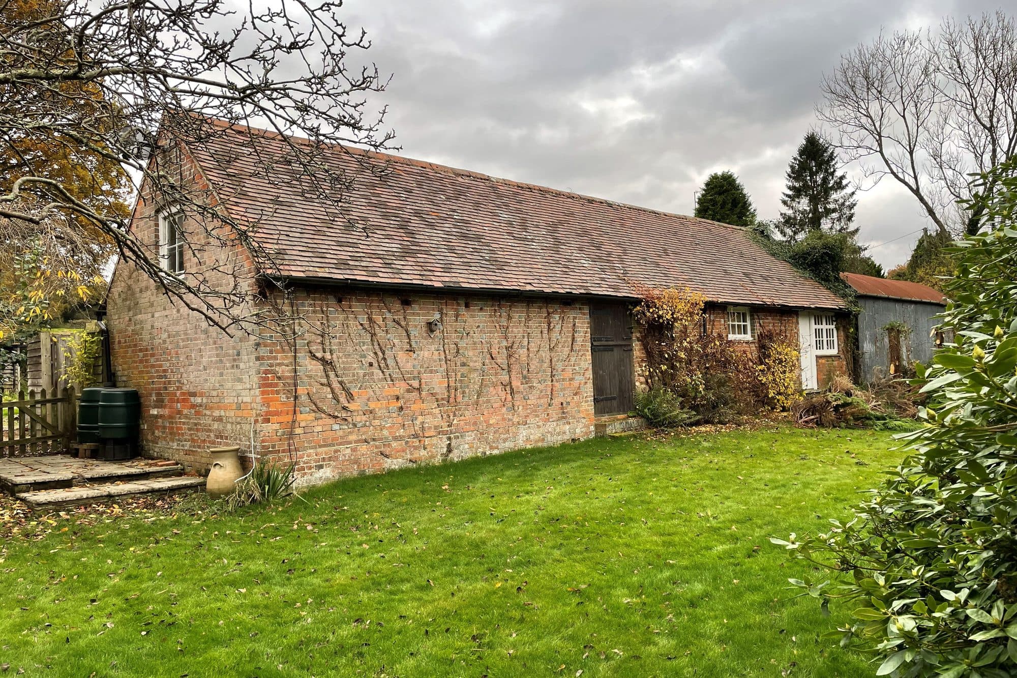 A long, single-storey brick barn with a clay tile roof across an autumn lawn