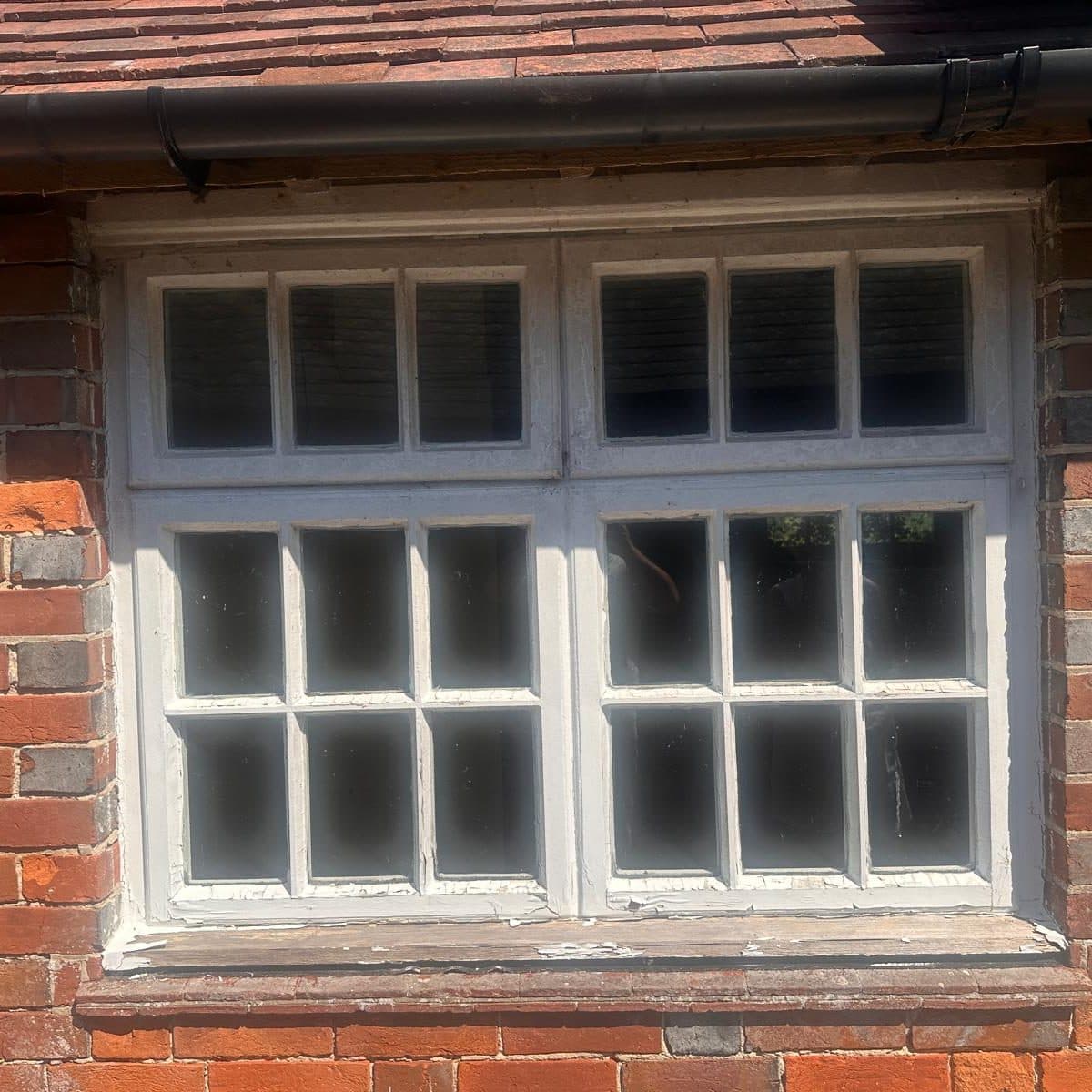 A painted multi-pane timber casement window set in red brickwork