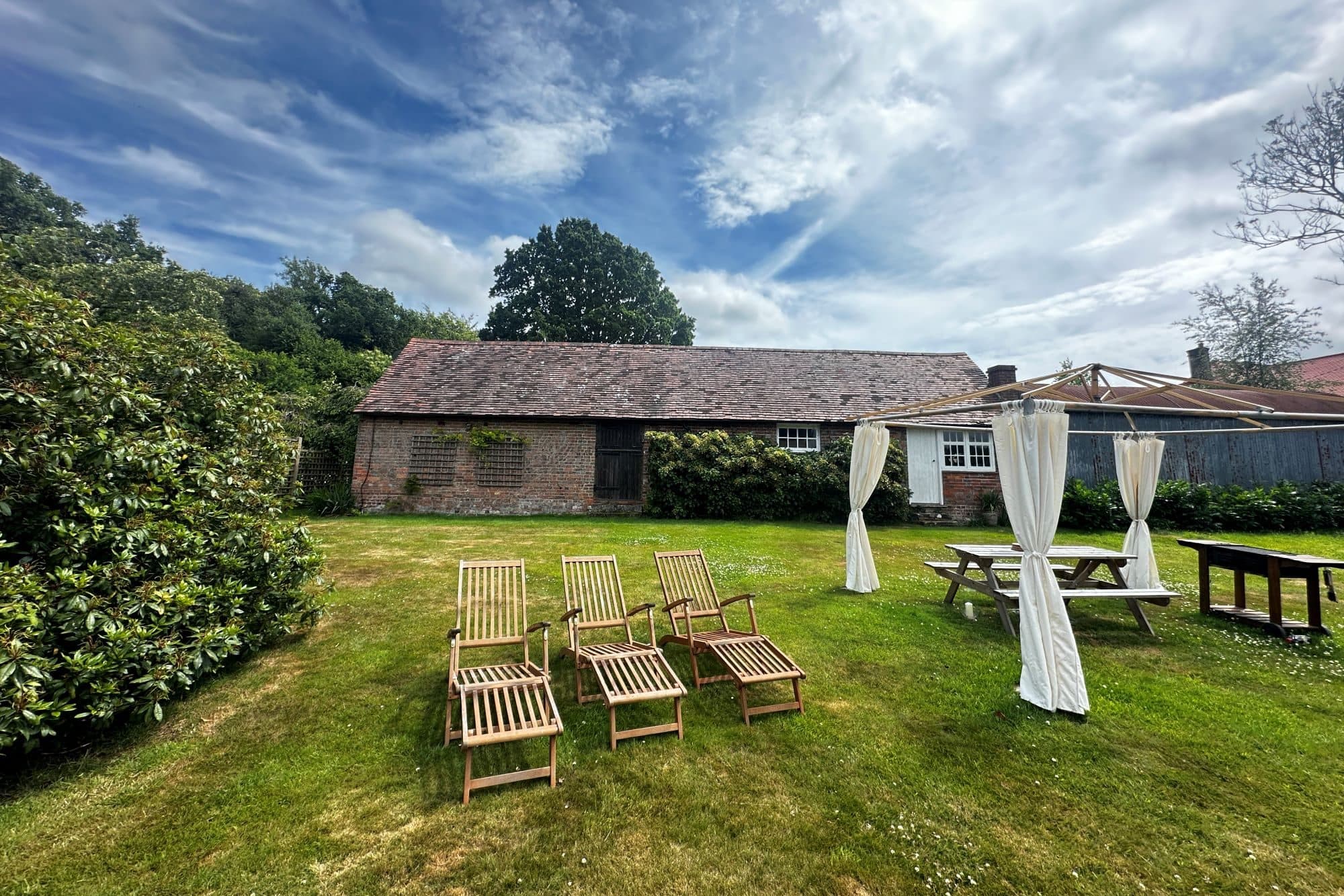 Garden loungers and a white canopy on a summer lawn, with the long brick barn beyond