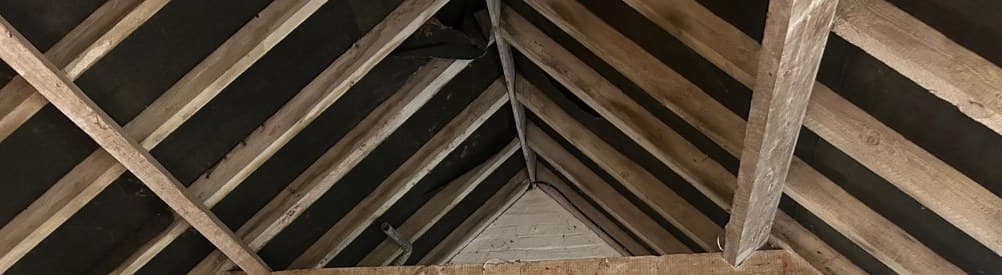 Timber coupled rafters and a tie beam under a clay tile roof, painted brick walls below