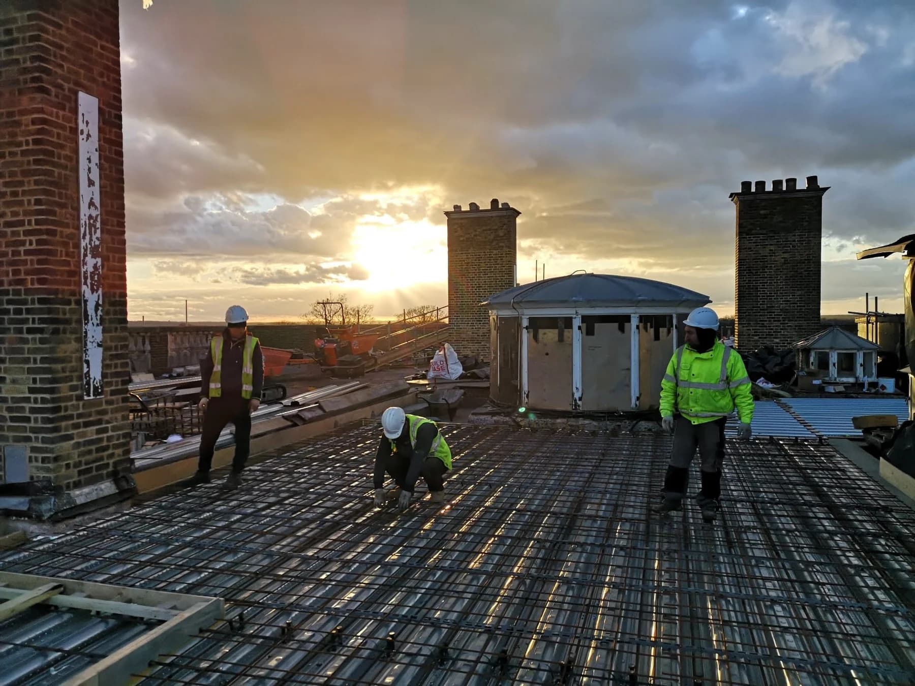 Workers on the roof at sunset between brick chimney stacks and a lantern structure