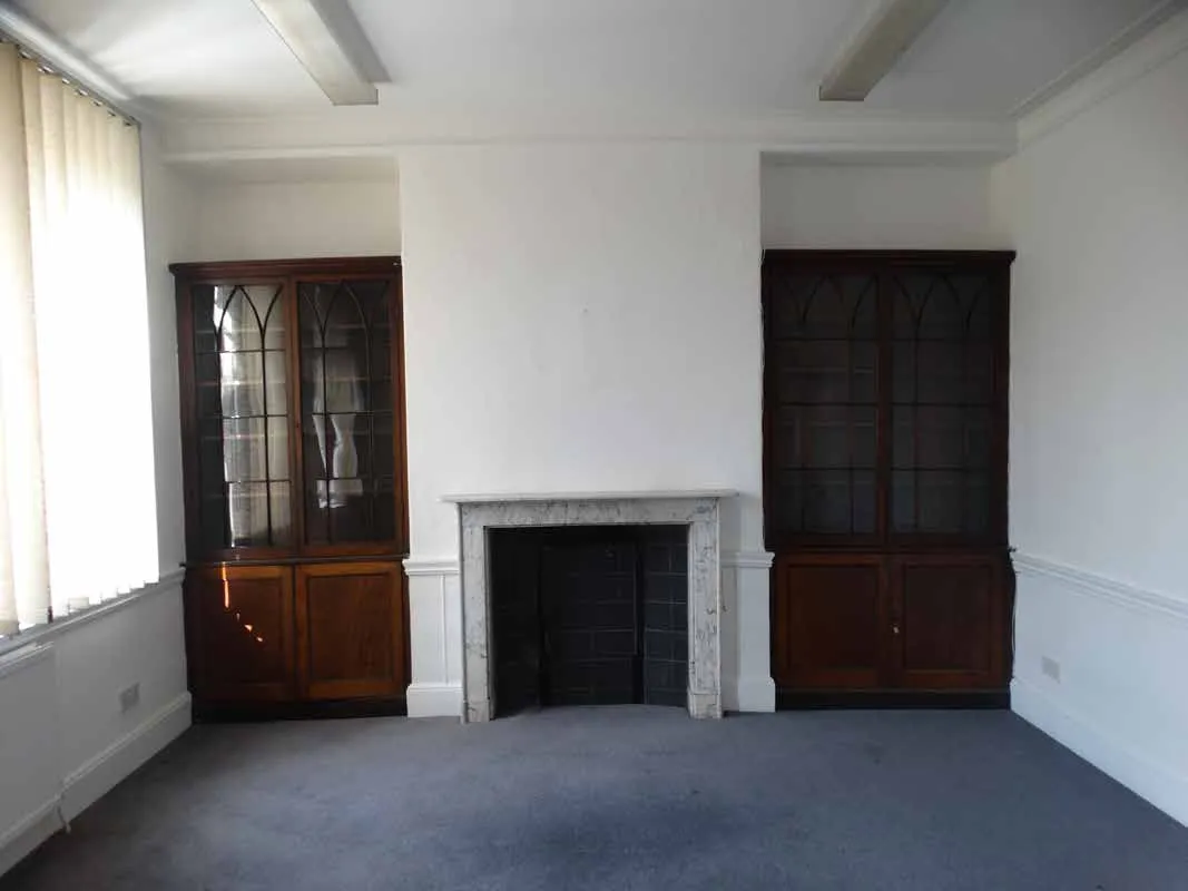 A white marble fireplace set between a pair of late Georgian mahogany bookcases at Bluecoats House, Hertford