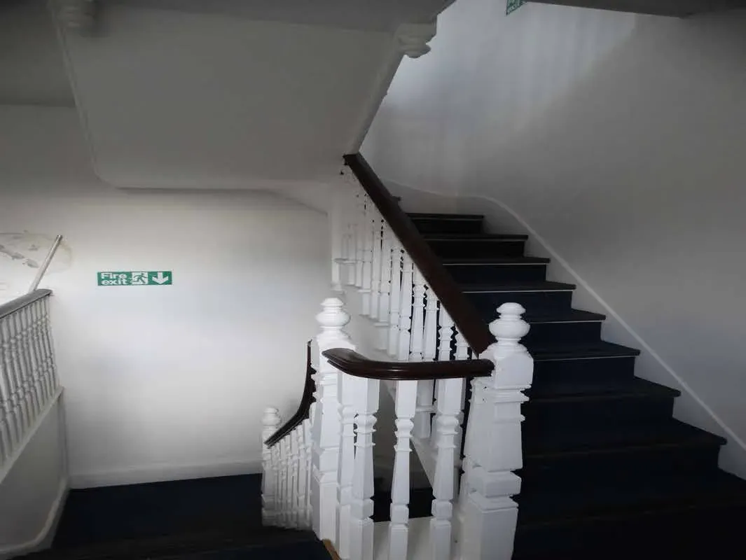 The open-well stair at Bluecoats House, with white turned balusters and a dark handrail rising past an exit sign